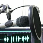 Mikrophon in der Nahaufnahme. Dahinter ein Aufnahmeprogramm auf dem Bildschirm