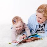 Frau mit Baby auf einer weißen Plüschdecke udn einem Kinderbuch
