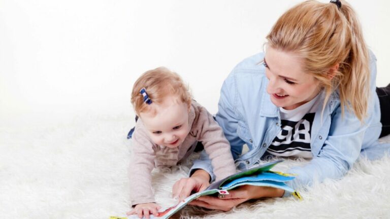 Frau mit Baby auf einer weißen Plüschdecke udn einem Kinderbuch