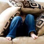 Kind auf Couch versteckt in drei Kissen.