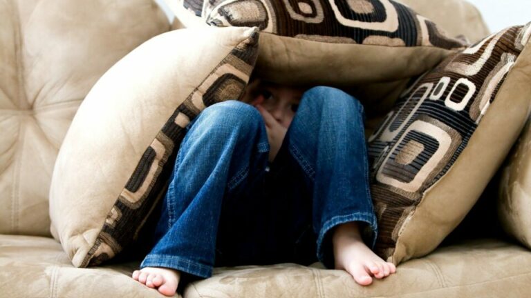 Kind auf Couch versteckt in drei Kissen.