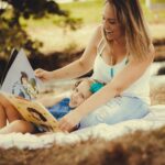 Frau mit Kind im Park liest aus einem Kinderbuch vor