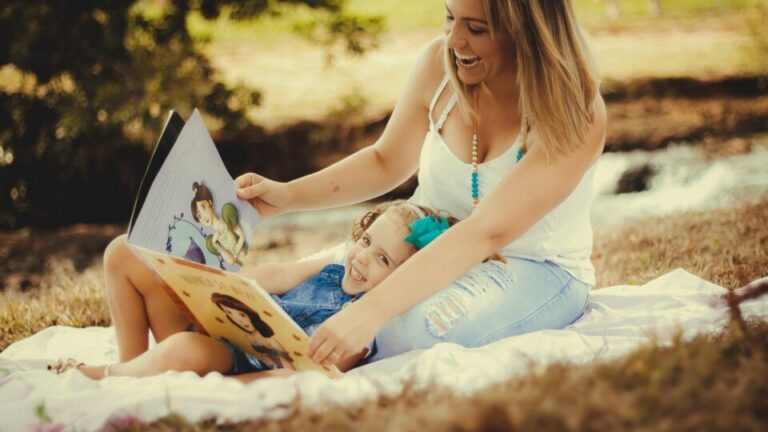 Frau mit Kind im Park liest aus einem Kinderbuch vor