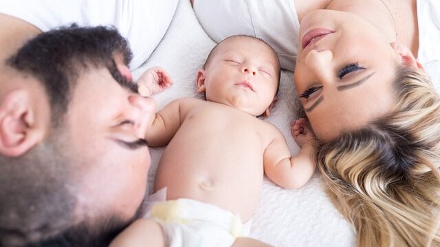 Familie Kopf an Kopf. Dazwischen ein Baby.
