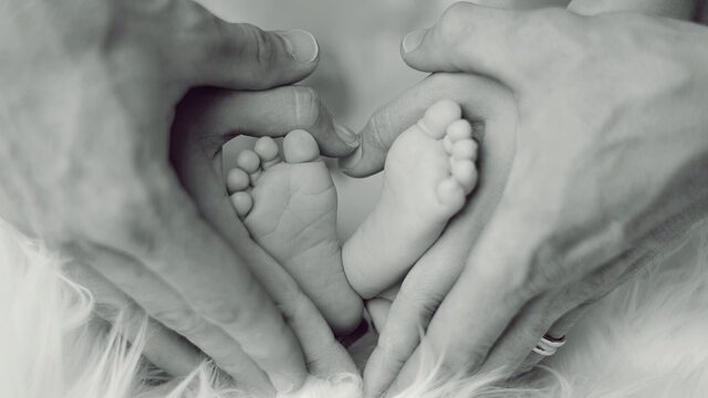 Schwarzweißbild Mann und Frau halten Füßchen ihres Babies. Die ineinanderglegten Hände erinnern an ein Herz
