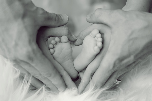 Schwarzweißbild Mann und Frau halten Füßchen ihres Babies. Die ineinanderglegten Hände erinnern an ein Herz