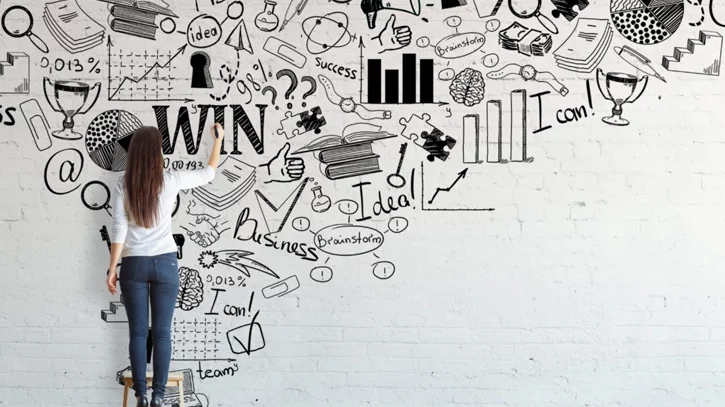 Frau zeichnet divers Symbole, die allesamt mit Statistik, Business, Erfolg, Ideen, etc zu tun haben an die Wand