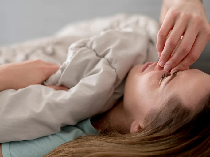 Frau im Bett fasst sich mit schmerzverzerrtem Blick an die Stirn.