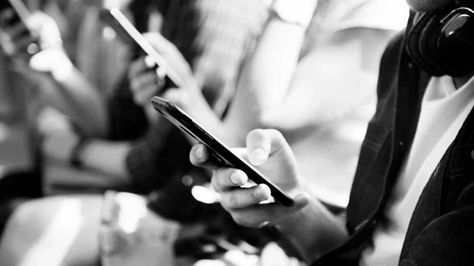 Schwarz-Weiß-Bild - Drei Personen mit Smartphones sitzen in einer Reihe und spielen mit dem Handy.