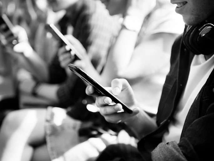 Schwarz-Weiß-Bild - Drei Personen mit Smartphones sitzen in einer Reihe und spielen mit dem Handy.