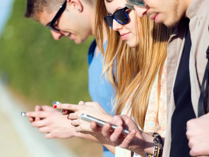 Drei Personen mit Sonnenbrille und Smartphones stehen in einer Reihe und spielen mit dem Handy.