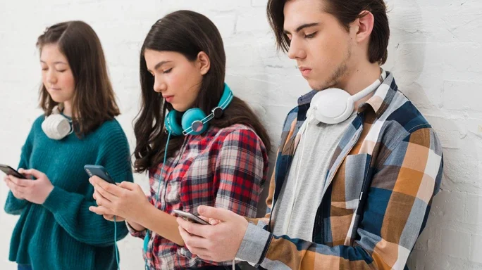 Drei Jungendliche mit Kopfhörern und Smartphones stehen in einer Reihe und spielen mit dem Handy.