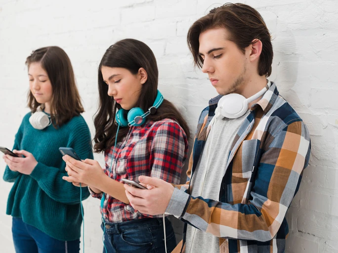Drei Jungendliche mit Kopfhörern und Smartphones stehen in einer Reihe und spielen mit dem Handy.