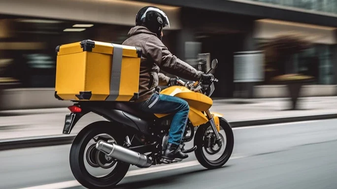 Lieferdienste - Man sieht einen Leiferanten auf einem Motorrad mit gelber Lebensmittelbox auf dem Gepäckträger