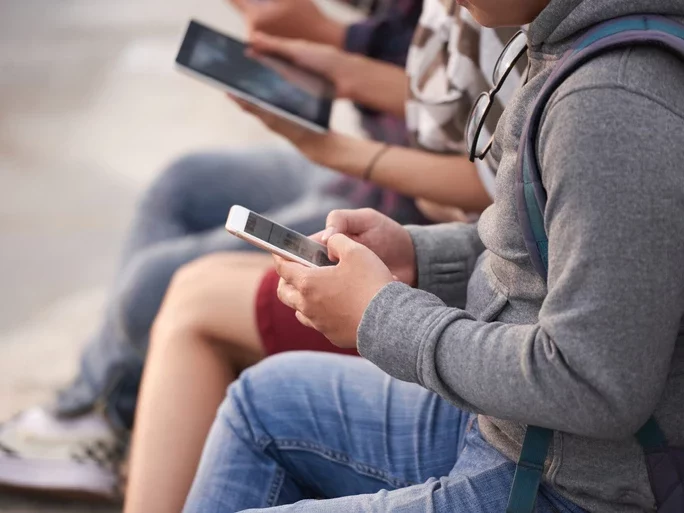 Nahaufnahme von Personen, die in einer Reihe sitzen und diversen mobile Geräten wie Tablets und Smartphones in ihren Händen halten und bedienen.