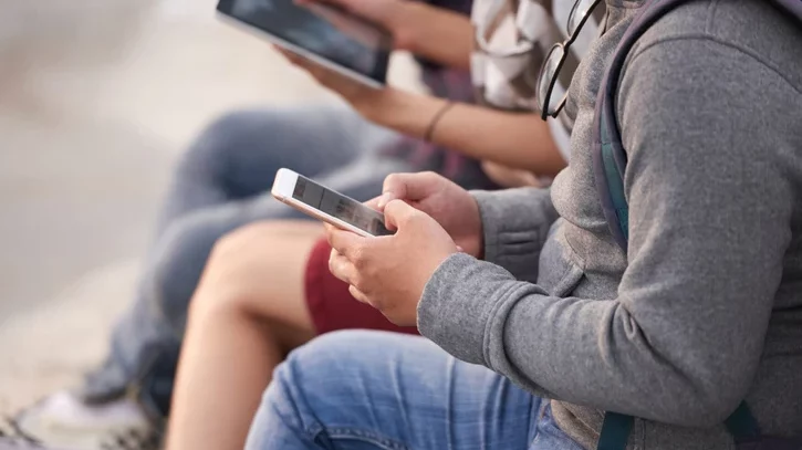 Nahaufnahme von Personen, die in einer Reihe sitzen und diversen mobile Geräten wie Tablets und Smartphones in ihren Händen halten und bedienen.