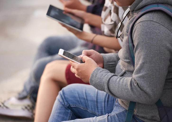 Nahaufnahme von Personen, die in einer Reihe sitzen und diversen mobile Geräten wie Tablets und Smartphones in ihren Händen halten und bedienen.