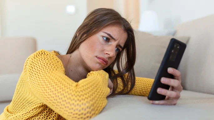 Frau sieht unglücklich in ein Handy. Beispielbild zur Hassrede im Interneet