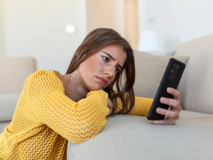 Frau sieht unglücklich in ein Handy. Beispielbild zur Hassrede im Interneet