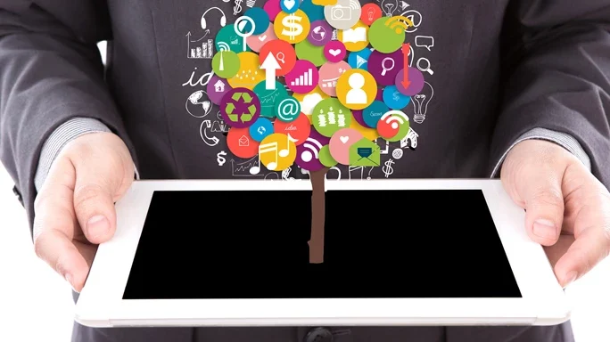 Massenkommunikationstrends Ein Mann hält ein Tablet, aus dem diverse Icons als Baum symbolisiert sind.