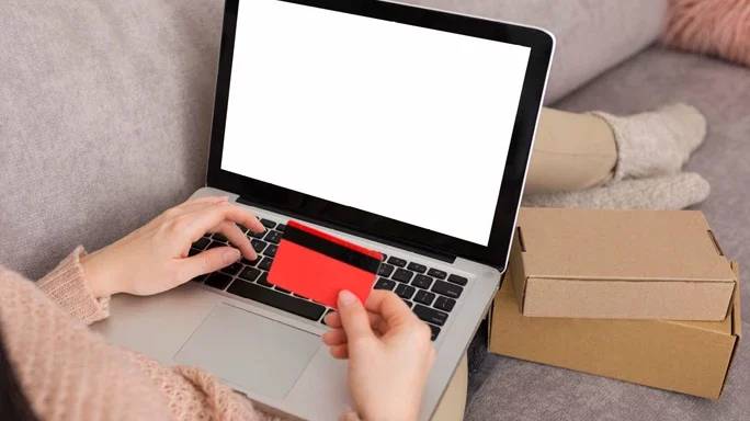 Frau auf der Couch beim online shoppen hält eine Kreditkarte in der Hand