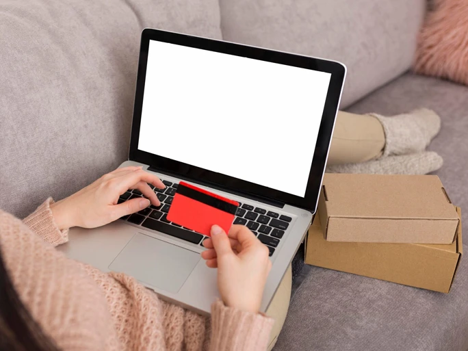 Frau auf der Couch beim online shoppen hält eine Kreditkarte in der Hand