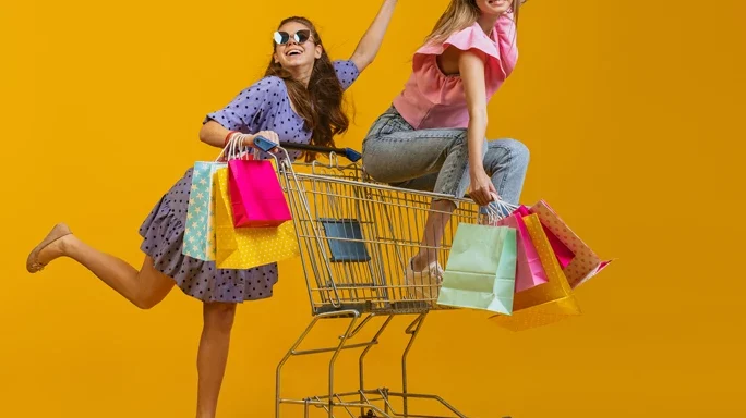 Zwei Mädchen beim shoppen. Eine sitzt in einem Einkaufswagen, die andere schiebt den Wagen