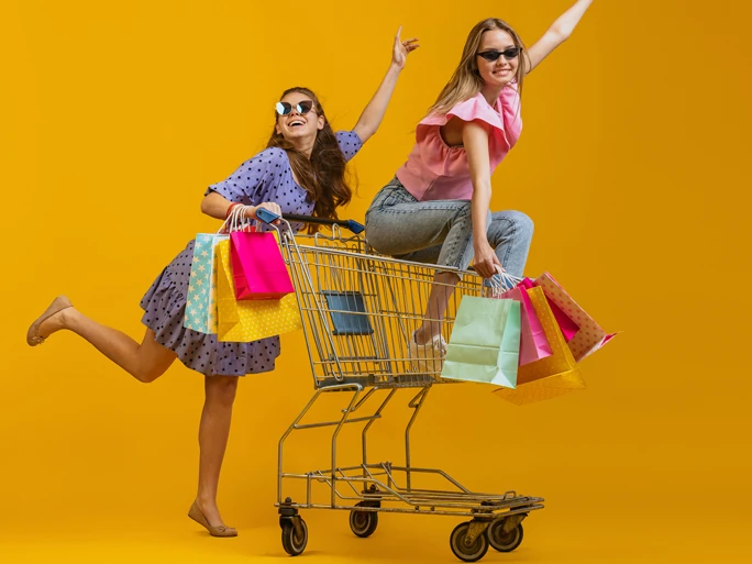 Zwei Mädchen beim shoppen. Eine sitzt in einem Einkaufswagen, die andere schiebt den Wagen