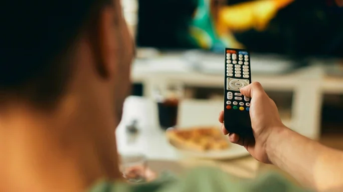 Mann sitzt auf Couch mit Fernbedienung in der Hand