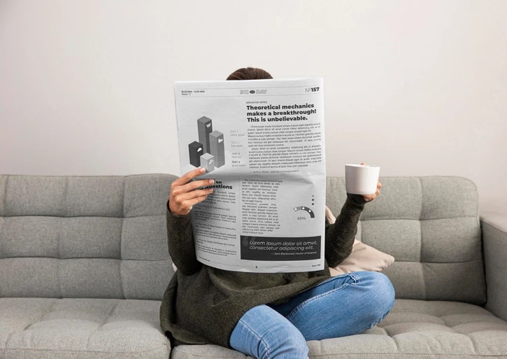 Person sitzt mit Zeitung und Kaffee auf der Couch