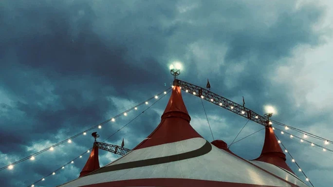 Man sient das Dach eines Zirkuszelts mit grauen Wolken am Himmel