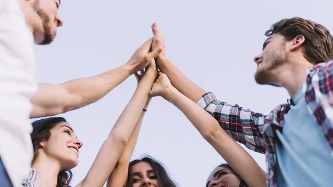 Jugendliche in Deutschland. 5 Personen stehen im Kreis und geben sich alle ein High-Five.
