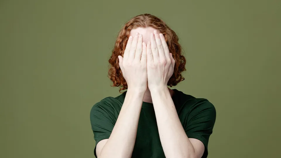 Rothaarige Frau in einem grünen Tshirt hält sich die Hände vors Gesicht