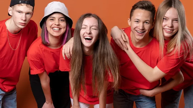 Fünf Teenager, drei Mädchen, zwei Jungs mit roten T-Shirts lachen in die Kamera