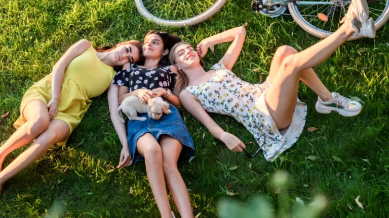 Drei Frauen liegen auf einer sommerlichen grünen Wiese neben einem Fahrrad.