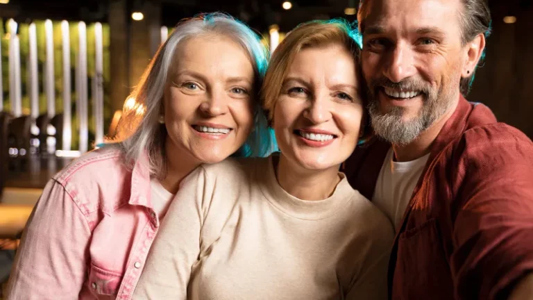 Zwei Frauen und ein Mann mittleren Alters schauen fröhlich in die Kamera.