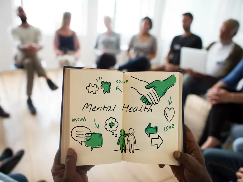 Eine Diskussionsgruppe man sieht aus der Ego-Perspektive ein aufgeschlagenes Notizbuch mit Illustrationen zum Thema Mental Health.