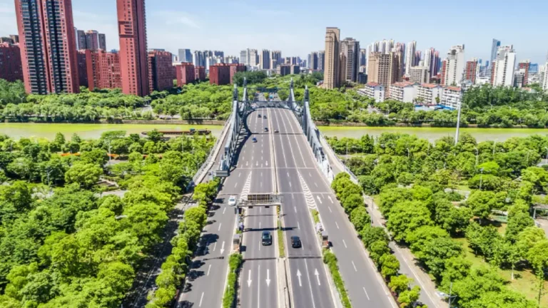 Eine achtspurige Strasse über eine Brücke in einer Stadt. Links und rechts der Strasse ist es bis zum Fluß sehr grün bewachsen