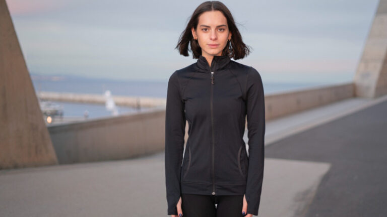 Frau in schwarzer Sportkleidung steht auf einer Pier am Meer.