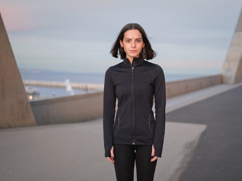 Frau in schwarzer Sportkleidung steht auf einer Pier am Meer.