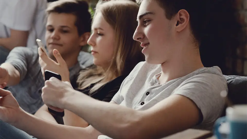 Zwei Jungs und ein Mädchen mit Smartphones auf einer Couch