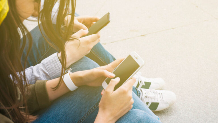 Zwei Jugendliche mit Smartphone sitzen auf dem Boden.
