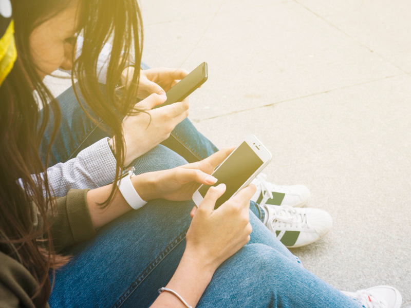 Zwei Jugendliche mit Smartphone sitzen auf dem Boden.