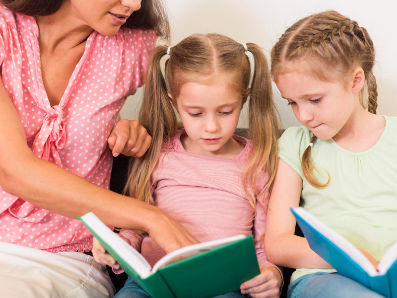 Mutter mit ihren zwei Töchtern, die Mädchen halten jeweils ein Buch in den Händen und lesen gespannt.