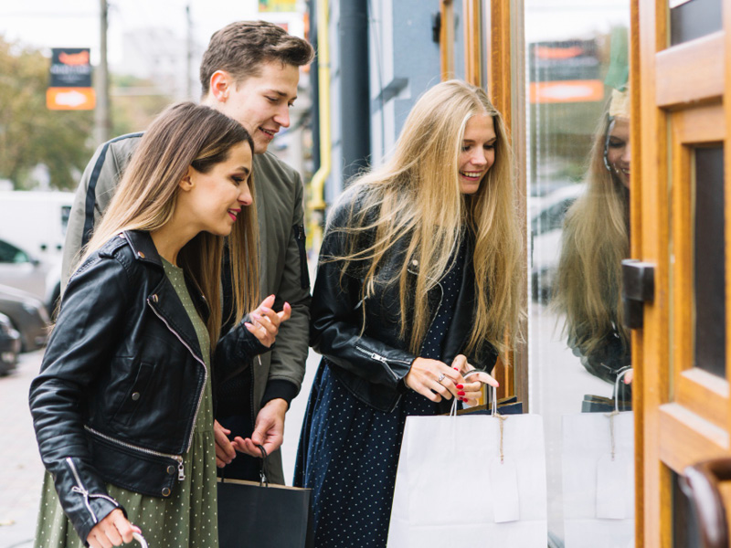 Zwei junge Frauen und eine Mann blicken in ein Schaufenster.