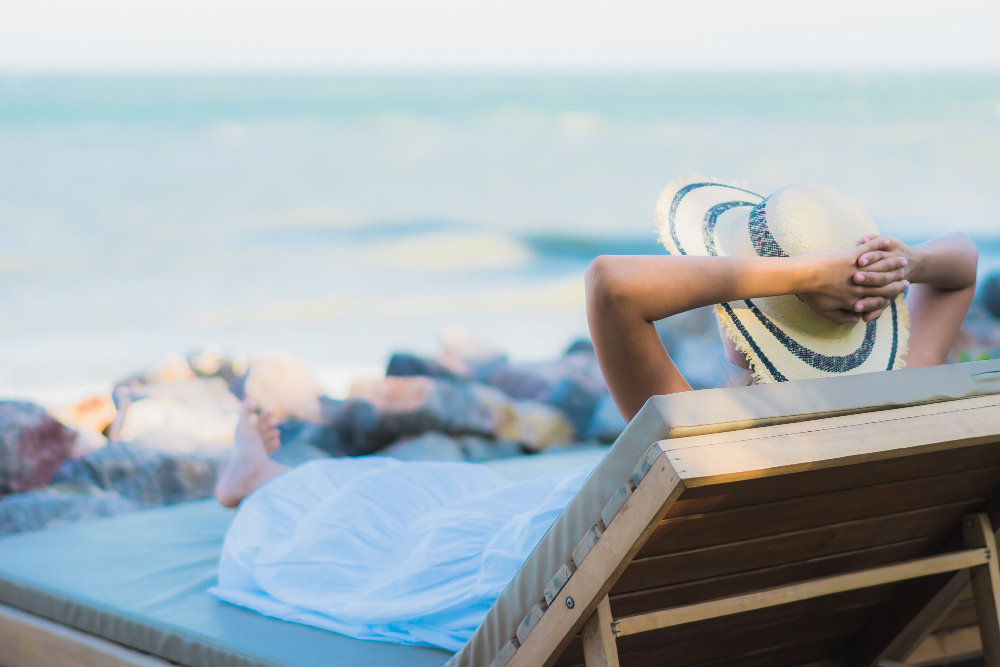 frau auf liege am strand , hände über den kopf entspannung