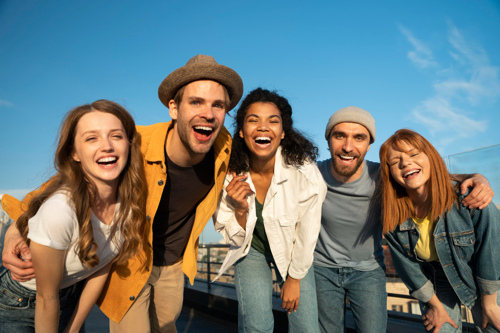 Fünf junge Menschen lachen fröhlich zusammen vor blauem Himmel.