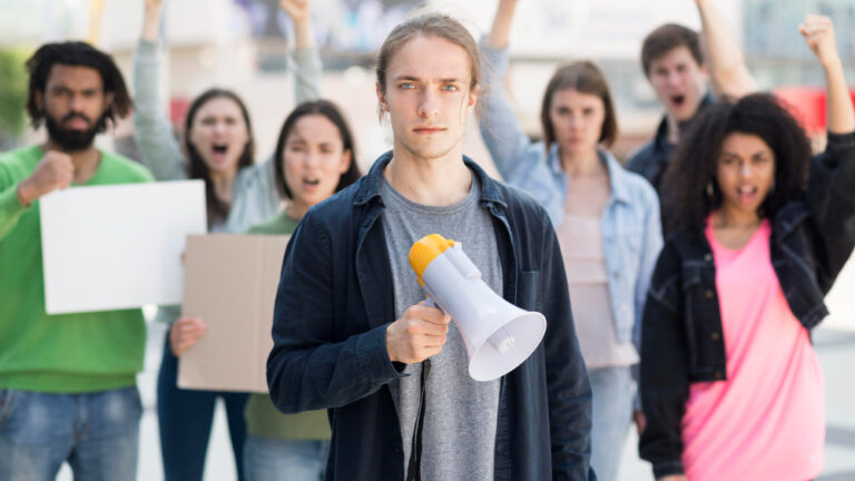 Gruppe von Menschen mit Schildern demonstriert, vorne steht ein Mann mit Megafon.