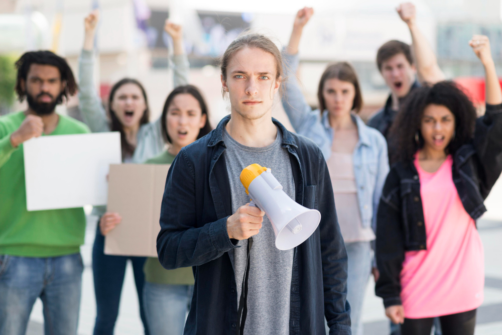 Gruppe von Menschen mit Schildern demonstriert, vorne steht ein Mann mit Megafon.