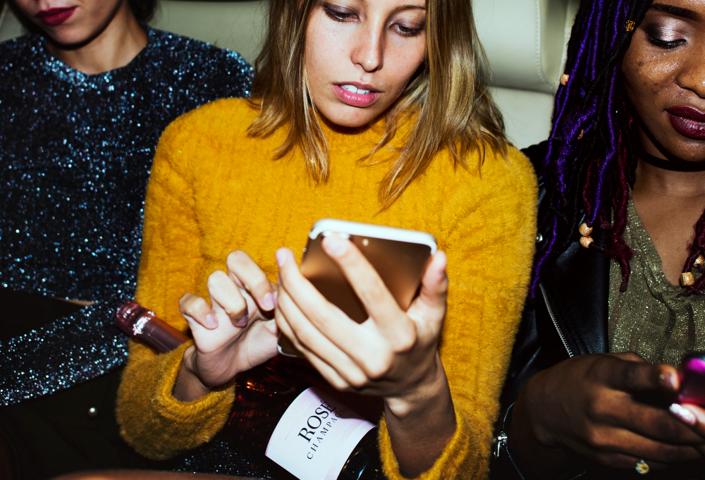 Frau in der Mitte zwischen zwei Personen, sie schaut auf ihr Handy.